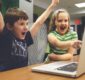 Photo of 2 children excitedly watching a video on a laptop.