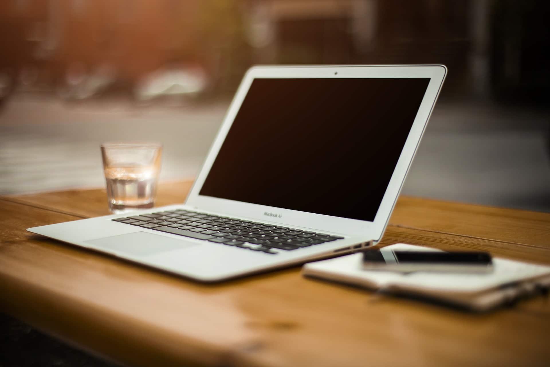 Photo of a laptop computer on a wooden table with a notepad and a glass of water.