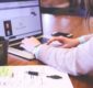 Photo of a woman working on a laptop with a notebook and coffee mug nearby.