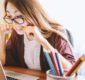 Photo of an irritated woman biting a pencil while using a laptop.