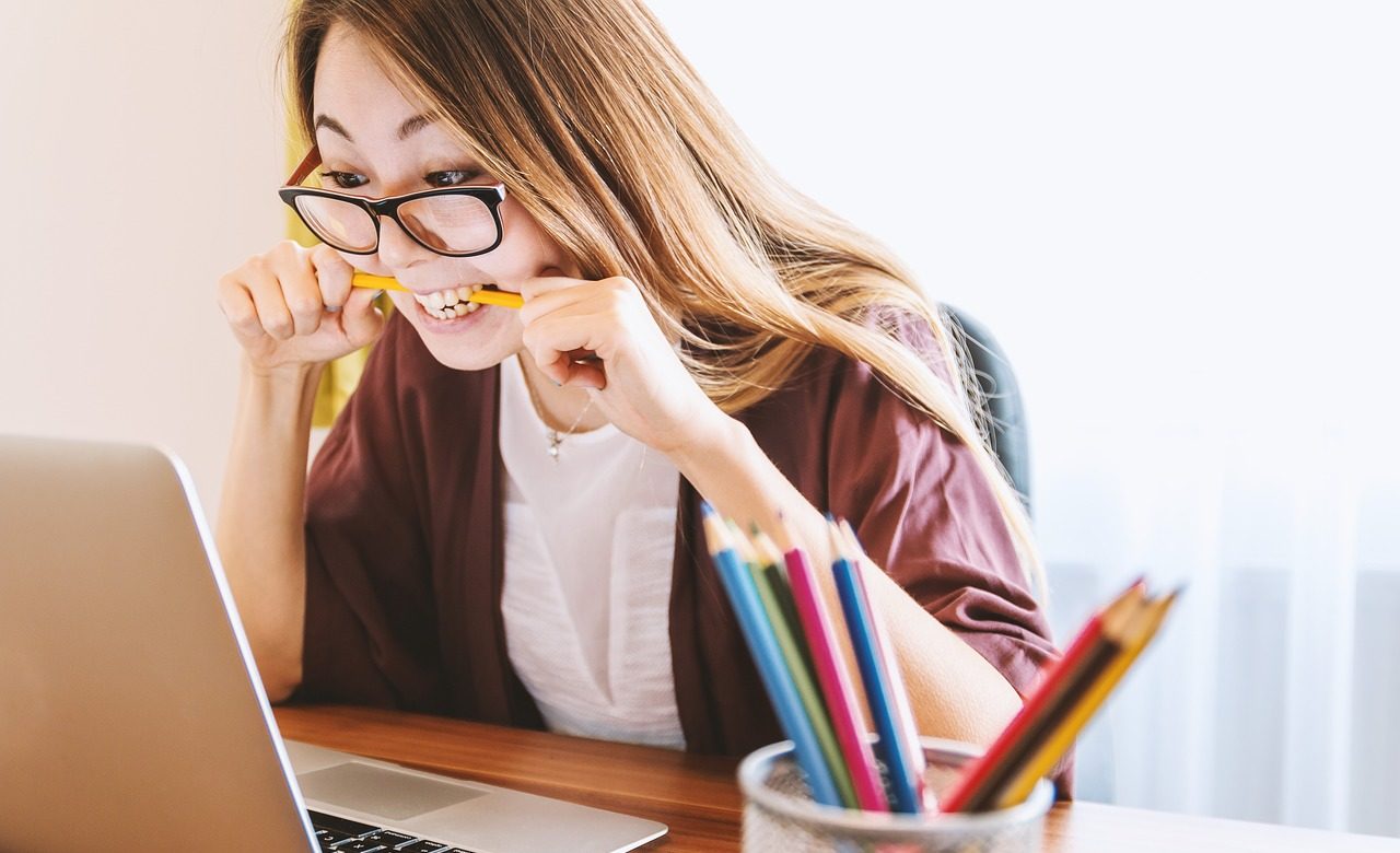 Photo of an irritated woman biting a pencil while using a laptop.